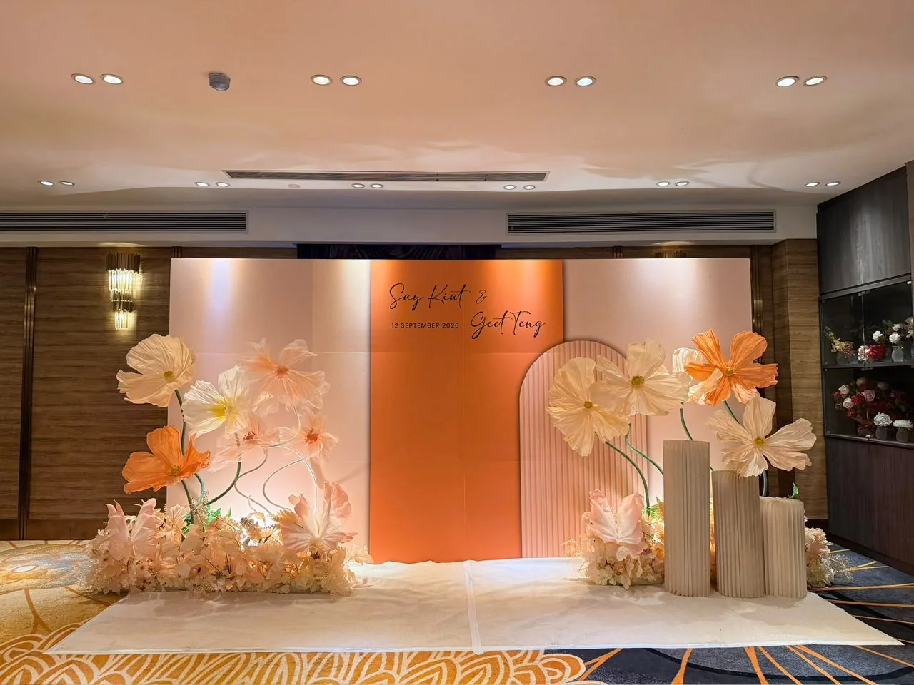Warm peach wedding backdrop with oversized flowers and soft lighting